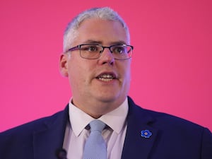 Headshot of Gavin Robinson speaking, with pink background