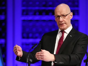 John Swinney speaking in front of a purple background