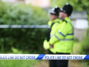 Uniformed police officers standing within an area cordoned off by blue and white police tape