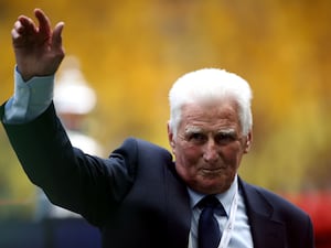 Former Manchester City captain and manager Tony Book, wearing a suit, waves to someone at an event