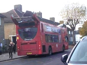 A red bus on a road, with the roof torn off