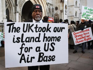 A Chagossian stands outside the High Court with a sign reading 'The UK took our island home for a US Air Base'