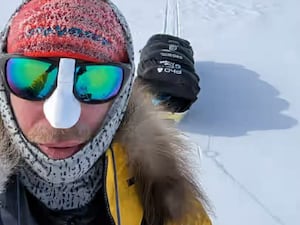 Johnny Huntington wearing sunglasses and a snood standing in front of his sled in Antarctica