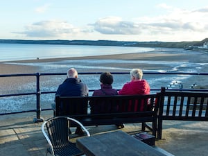 Three older people sitting on a bench overlooking a beach