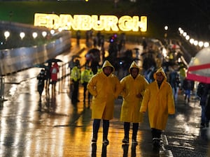 Revellers in yellow rain coats with the word 'Edinburgh' written in lights behind them