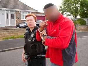 A Cleveland Police officer escorts a man - with face blurred - arrested in Middlesbrough