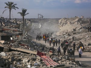 People walk along a road surrounded by destroyed buildings