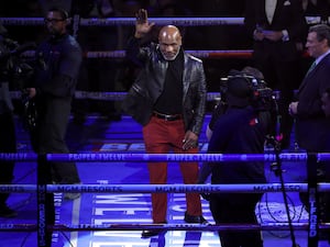 Mike Tyson stands in a boxing ring with his arm raised