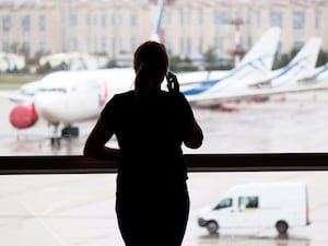 A silhouette of a woman talking on a mobile phone in an airport terminal, with several planes in the background