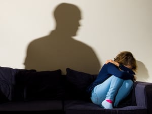 Woman with head in hands on couch with silhouette of man in background