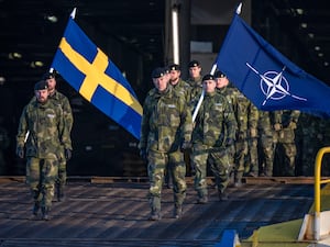 Swedish soldiers holding Swedish and Nato flags disembarking in the port of Riga, Latvia