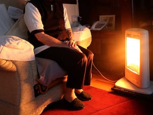 An old person sitting in front of an electric fire