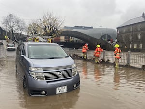 A car in flood water with firefighters standing close by