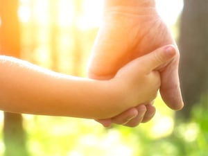 An adult holding a child's hand (Alamy/PA)