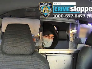 Man wearing facemask and hat looking through partition in a cab