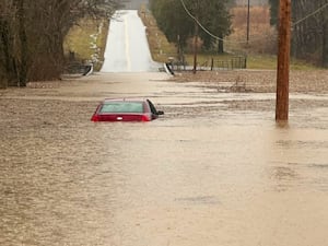 A car mostly submerged in flood water on a road