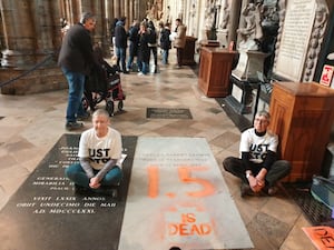 Two women sitting cross-legged during Just Stop Oil protest at Charles Darwin's grave in Westminster Abbey. '1.5 is dead' is painted in orange on his grave