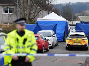 A police officer stands in front of a cordon and forensic tent