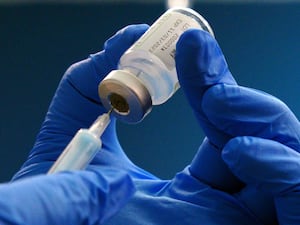 Blue-gloved hands holding needle in a vial of the Moderna spikevax Covid vaccine