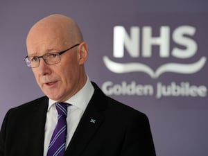 John Swinney speaking in front of an NHS sign