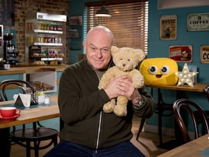 Ross Kemp smiling while holding a teddy, in the EastEnders cafe set