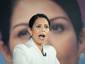 Dame Priti Patel speaking, in front of a large image of herself