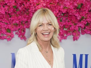 Headshot of Zoe Ball smiling, in front of pink flowers