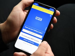 A person holding a mobile phone displaying the NHS app.