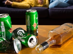 Empty cans and bottles on a table, with a person slumped on a sofa in the background