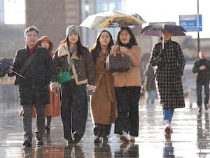 People shelter from the rain beneath an umbrella as they cross London Bridge in central London.