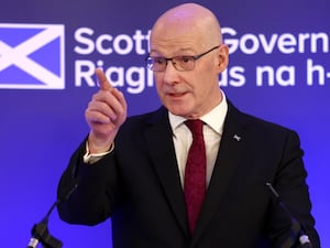 John Swinney pointing while speaking in front of Scottish Government signage