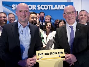 Stephen Flynn and John Swinney smiling in front of SNP supporters and signage