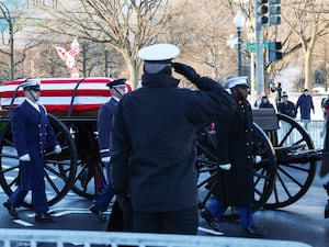 A serviceman salutes as the flag-draped casket of former president Jimmy Carter passes by on a horse-drawn carriage