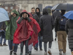 People cross the Millennium Bridge in London carrying umbrellas