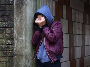 Young person leaning against a wall with hands covering their face