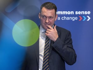 Russell Findlay standing in front of Tory signage, with one finger on his lips