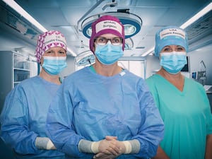 Three medics in caps, scrubs and facemasks in a hospital theatre