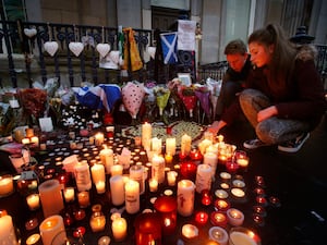 People look at dozens of lit candles on a street