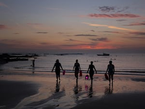 The silhouettes of four swimmers walking from the sea before sunrise