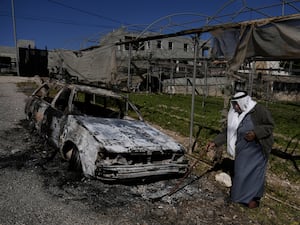 A Palestinian stands beside a torched car in the aftermath of an attack by Israeli settlers in the West Bank village of Jinsafut