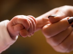 A baby gripping a woman's finger