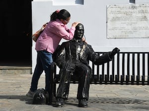 A woman embraces a statue of a seated Jose Gregorio Hernandez