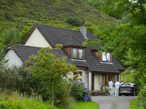 Police outside a house partially covered by green foliage