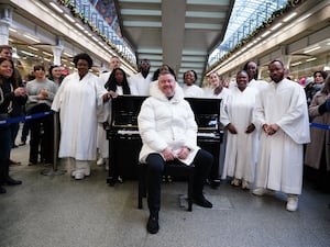 Tony Mortimer sat next to a piano among a crowd at St Pancras International station