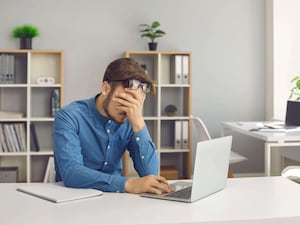 Stressed man sitting at laptop with hand on his face