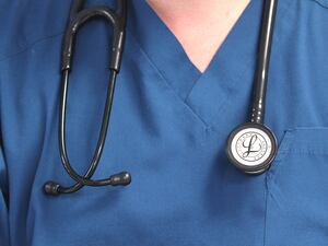 A person wearing a blue tunic, with a stethoscope round their neck