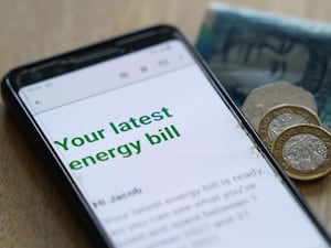 An energy bill is displayed on a smartphone screen next to bank notes and coins