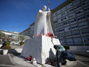 A woman kneels at the foot of a statue of late Pope John Paul II outside the Agostino Gemelli Polyclinic in Rome