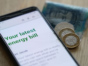 Energy bill displayed on a smart phone, with coins and banknotes beside it