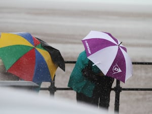 Two people holding umbrellas in the wind at the seaside